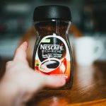 Faceless person taking glass jar filled with granulated instant coffee from wooden table in kitchen